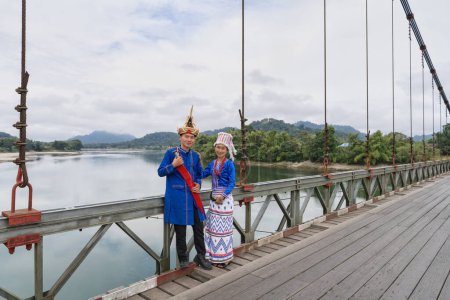 Foto de Una joven pareja Rawang, vestida con vibrante atuendo tradicional, se encuentra en el puente Kaungmulone, Putao, con el sereno río Mali Kha fluyendo suavemente en el estado de Kachin, Myanmar - Imagen libre de derechos