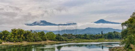 Foto de Una vista panorámica del sereno río Mali Kha desde el puente Kaungmulone, envuelto por montañas brumosas y exuberante vegetación en Putao, estado de Kachin, Myanmar - Imagen libre de derechos