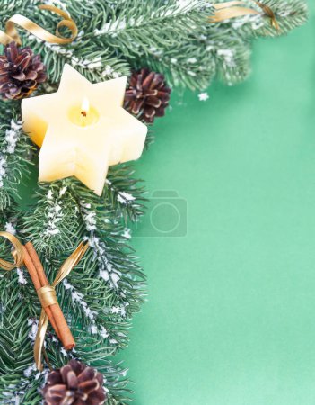 Téléchargez les photos : Les branches d'un sapin de Noël artificiel, une bougie, des bâtons de cannelle et d'autres décorations de Noël sont placées sur un fond vert - en image libre de droit