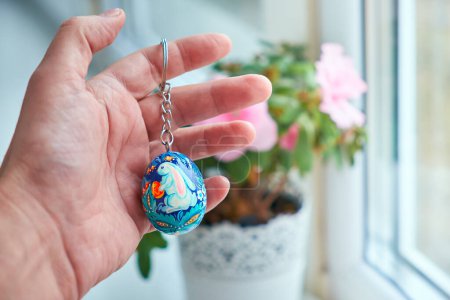 Photo for Keychain in the form of Ukrainian Easter egg with Petrykivka painting in the palm. Hand-painted wooden decor. - Royalty Free Image
