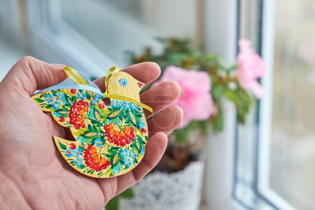 Photo for Easter ornament bird with Petrykivka painting in the palm on the window background. Ukrainian hand painted wooden ornament. - Royalty Free Image