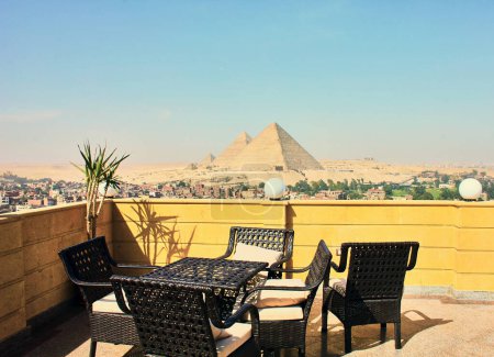 Table avec quatre chaises sur terrasse donnant sur les pyramides égyptiennes