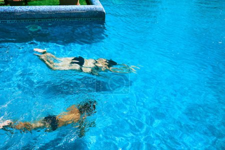 Téléchargez les photos : Mère et fils nagent sous l'eau dans une piscine bleue, profitant du soleil d'été dans une station hôtelière. - en image libre de droit