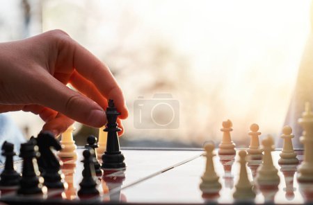 El tablero de ajedrez está hecho de madera. Persona jugando ajedrez en la naturaleza. La persona sostiene a un rey negro en su mano.