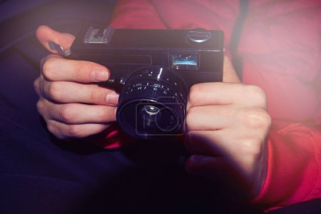 Nahaufnahme einer Kleinbildkamera, die in Händen gehalten wird. Klassisches Modell aus den 90er Jahren, mit schwarzem Gehäuse und Linse. Das Foto fängt die Nostalgie der Filmfotografie und die Aufregung ein, den Moment in der Zeit einzufangen.