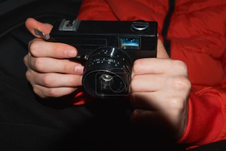 Nahaufnahme einer Kleinbildkamera, die in Händen gehalten wird. Klassisches Modell aus den 90er Jahren, mit schwarzem Gehäuse und Linse. Das Foto fängt die Nostalgie der Filmfotografie und die Aufregung ein, den Moment in der Zeit einzufangen.