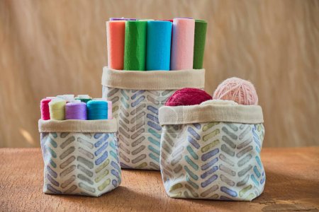 Colorful yarn and felt rolls in fabric storage basket on wooden table. Perfect for home decor, everyday life, and hygiene concepts. Boho style home decor. Craft supplies.