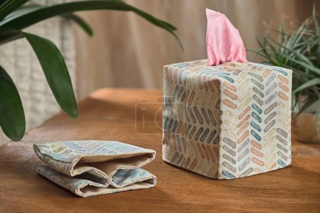 Tissue box with a pink tissue peeking out on a wooden table next to a plant. Perfect for home decor, everyday life, and hygiene concepts. Boho style home decor.