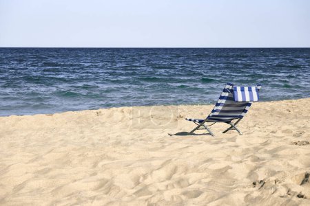 Entspannender blau-weiß gestreifter Strandkorb an einem Sandstrand. Einsamkeit an einem ruhigen Strand.