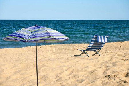 Relaxing beach scene with a blue and white striped beach chair and a striped umbrella. Solitude on a tranquil beach.