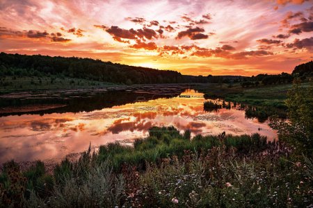 Ein ruhiger Sonnenuntergang über einem ruhigen See, mit leuchtenden Orange- und Rottönen, die sich im ruhigen Wasser spiegeln. Idyllische Szene.