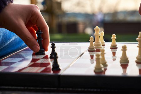 Photo for Person playing chess in nature. The person is holding a black king in their hand. A close-up of a chess player's hand holding a king piece, as if to protect the king. - Royalty Free Image