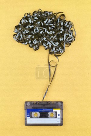 Konzept zum Schutz psychischer Gesundheit durch Musik. Vintage-Kassettenband mit belichtetem Klebeband in Form von Gehirn. Sonnenschein gelb Farbe Papier Hintergrund.