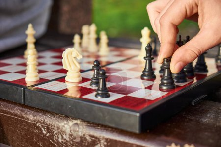 Person, die Schach in der Natur spielt. Nahaufnahme der Hand eines Schachspielers, der einen Turm hält und dabei ist, einen Zug zu machen.