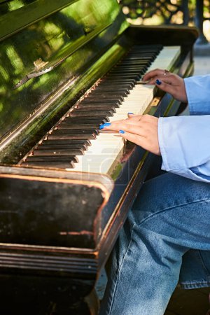 Photo of a woman in denim playing a vintage piano in a park on a warm sunny day. Her blue nails dance across the keys as she plays a beautiful melody.