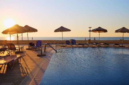 Lever de soleil serein sur une piscine tranquille entourée de verdure luxuriante et de chaises longues, invitant à la détente et à l'évasion.