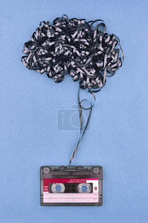 Concept with mental health protection by music. Vintage cassette tape with exposed tape in the form of brain. Chambray blue color paper background.