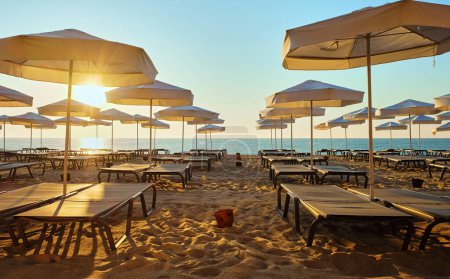 Entspannen am Strand. Eine Reihe weißer Liegestühle und Sonnenschirme am Sandstrand bei Sonnenaufgang.
