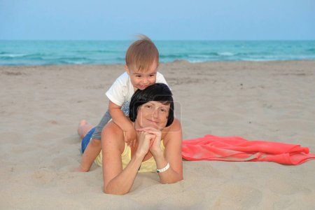 Eine fröhliche Mutter und ihr Sohn spielen an einem Sandstrand mit dem Meer im Hintergrund.