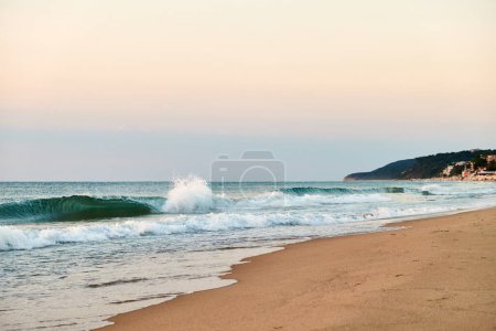 Eine ruhige Strandszene mit sanften Wellen, die bei Sonnenuntergang gegen das Ufer plätschern und ein faszinierendes Schauspiel der Schönheit der Natur schaffen.