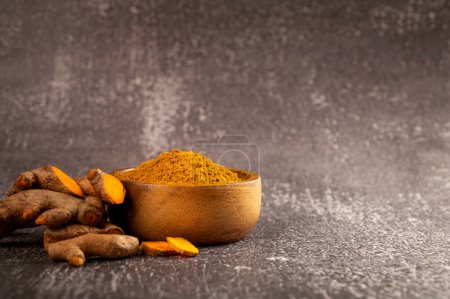 raw organic turmeric powder in a bowl on a dark stone background. copy space for text.