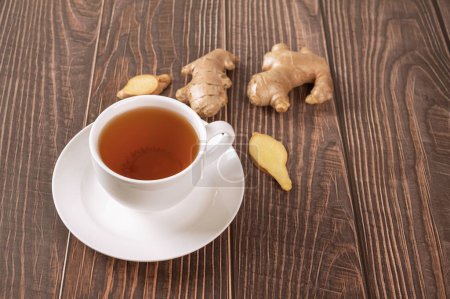 Téléchargez les photos : Tasse de thé au gingembre avec racine et tranches sur fond de bois. - en image libre de droit