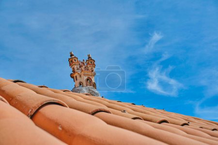 Foto de Un edificio con un techo rojo y una torre en la parte superior. El techo está hecho de baldosas y la torre está hecha de piedra. El cielo es azul y no hay nubes - Imagen libre de derechos