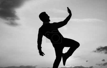 Téléchargez les photos : Silhouette of guy making selfie on phone and make step in sense of freedom on sunrise sky, future. - en image libre de droit
