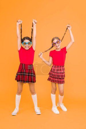 Photo for Summer fashion trend. Kids fashionable friends posing in sunglasses on yellow background. Summer fun. Summer accessory. Girls cute sisters similar outfits wear colorful sunglasses for summer season. - Royalty Free Image