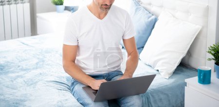 Téléchargez les photos : Mature homme utilisant ordinateur sur lit avec café. - en image libre de droit
