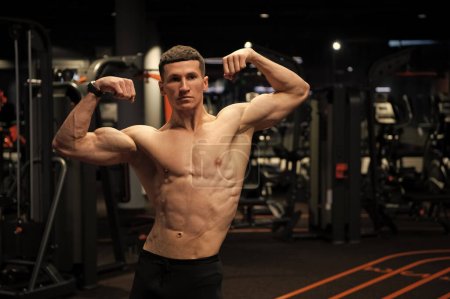 Hombre fuerte con músculos musculares de los brazos flexionados del torso mostrando bíceps dobles en el gimnasio, fuerza.