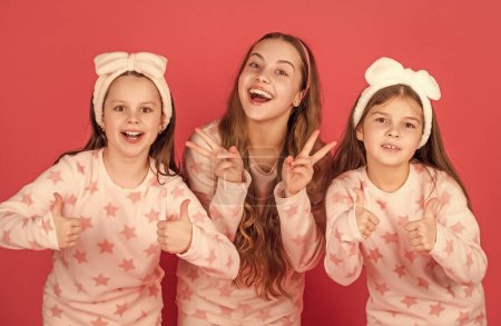 Photo for Giving thumbs and v-signs gestures. Happy children in homewear pink background. Kids homewear. - Royalty Free Image