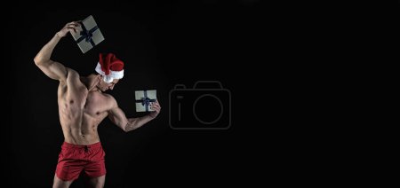 Photo for Muscular athlete in santa hat hold christmas present. muscular santa with christmas present isolated on black background. christmas banner of muscular athlete, copy space. merry christmas. - Royalty Free Image