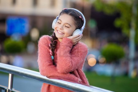 Téléchargez les photos : Fille heureuse écoutant de la musique. Adolescent mélomane écouter la chanson à l'extérieur. Adolescente écoute écouteurs avec les yeux fermés. - en image libre de droit