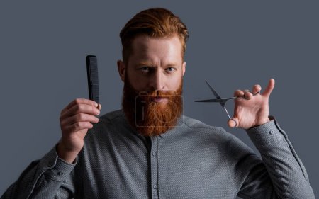 Photo for Man holding barber scissors and comb. barber with hairstyle. barber man making hairstyle isolated on grey background. barber man with scissors do hairstyle. man has beard and hairstyle in studio. - Royalty Free Image