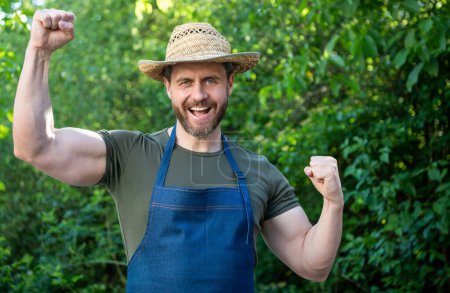 Foto de Hombre agricultor feliz en el sombrero de los agricultores y delantal hacer gesto ganador en el jardín aoutdoor. - Imagen libre de derechos