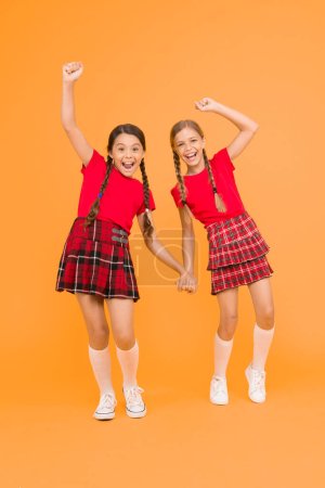 Photo for Time to relax. red fashion girls. english style fashion. happy little girls in checkered skirt. beauty look. happy children on yellow backdrop. childhood happiness. trendy school uniform. funny jump. - Royalty Free Image