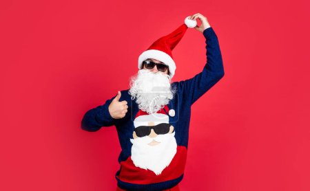 Téléchargez les photos : Heureux homme barbu dans santa claus chapeau et pull tricoté spectacle pouce vers le haut célébrer Nouvel An vacances d'hiver, nouvelle fête de l'année. - en image libre de droit