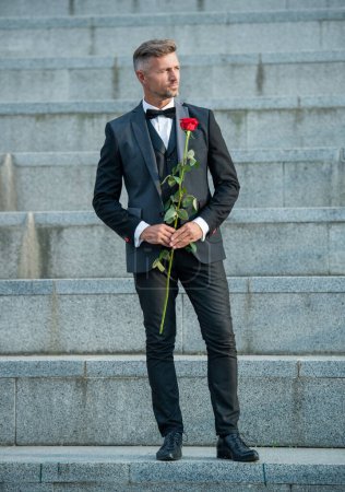 love rendezvous concept. full length of tuxedo man with love rose. flower gift for love day.