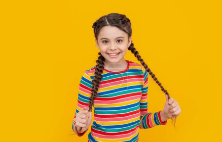 happy teen girl with braids on hair in studio. photo of teen girl having braids. childhood studio shot of teen girl has braids. teen girl with braids isolated on yellow background.