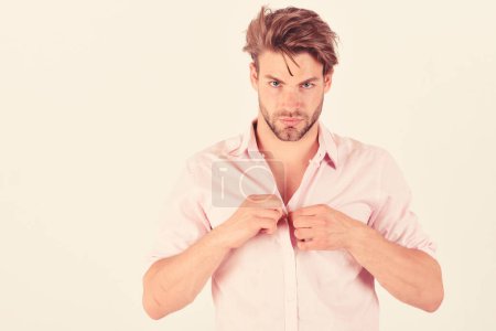 Photo for Fashion and confidence concept. Man with strict face isolated on white background, copy space. Guy with bristle in pink shirt and messy hair. Macho fastens or unfastens button. - Royalty Free Image