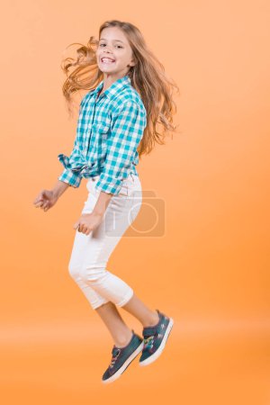 Girl bounce smiling on orange background. Happy girl jump with long blond hair.