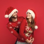 christmas time. happy new year couple in knitted sweater and santa claus hat. prepare for xmas party fun. happy holidays for young family. man and woman on red background. love.