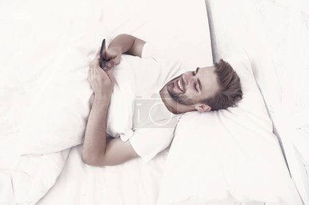 Photo for Set up morning alarm. Apps that help monitor sleep. Man use mobile phone in bed. Waking up. Application analyzes stages of sleep and wakes you up at optimal time. Provide deeper sleep analysis. - Royalty Free Image
