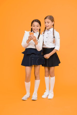 Photo for Internet is wonderful resource but access to it has hazards for kids. Girls school uniform using smartphone. Schoolgirls use mobile phone or smartphone to share photos. School application smartphone. - Royalty Free Image