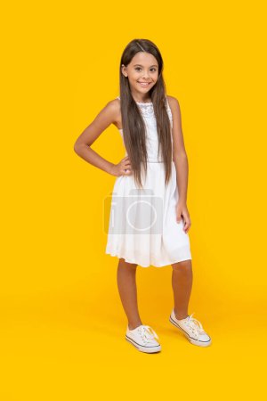 fröhliches Teenie-Kind in weißem Kleid steht auf gelbem Hintergrund.