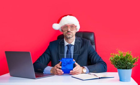 Téléchargez les photos : Mature avocat porter rouge santa claus chapeau et lunettes de fête tenir boîte cadeau. - en image libre de droit