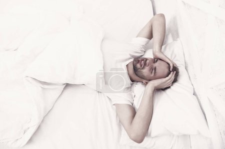 Photo for Sleep problems can lead to headaches in morning. Handsome man relaxing in bed. Snoring can increase risk headaches. Common symptom of sleep apnea. Causes of early morning headache. Migraine headaches. - Royalty Free Image