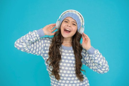 Photo for Cheerful small child knitted sweater and earphones. singing kid turquoise background. her favorite winter songs. happy girl enjoy winter playlist. music mood. song to motivate you in cold weather. - Royalty Free Image