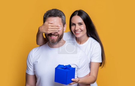 happy surprise couple with present in studio. holiday couple with present box. photo of couple with present for holiday surprise. mens day. couple with surprise present isolated on yellow background.